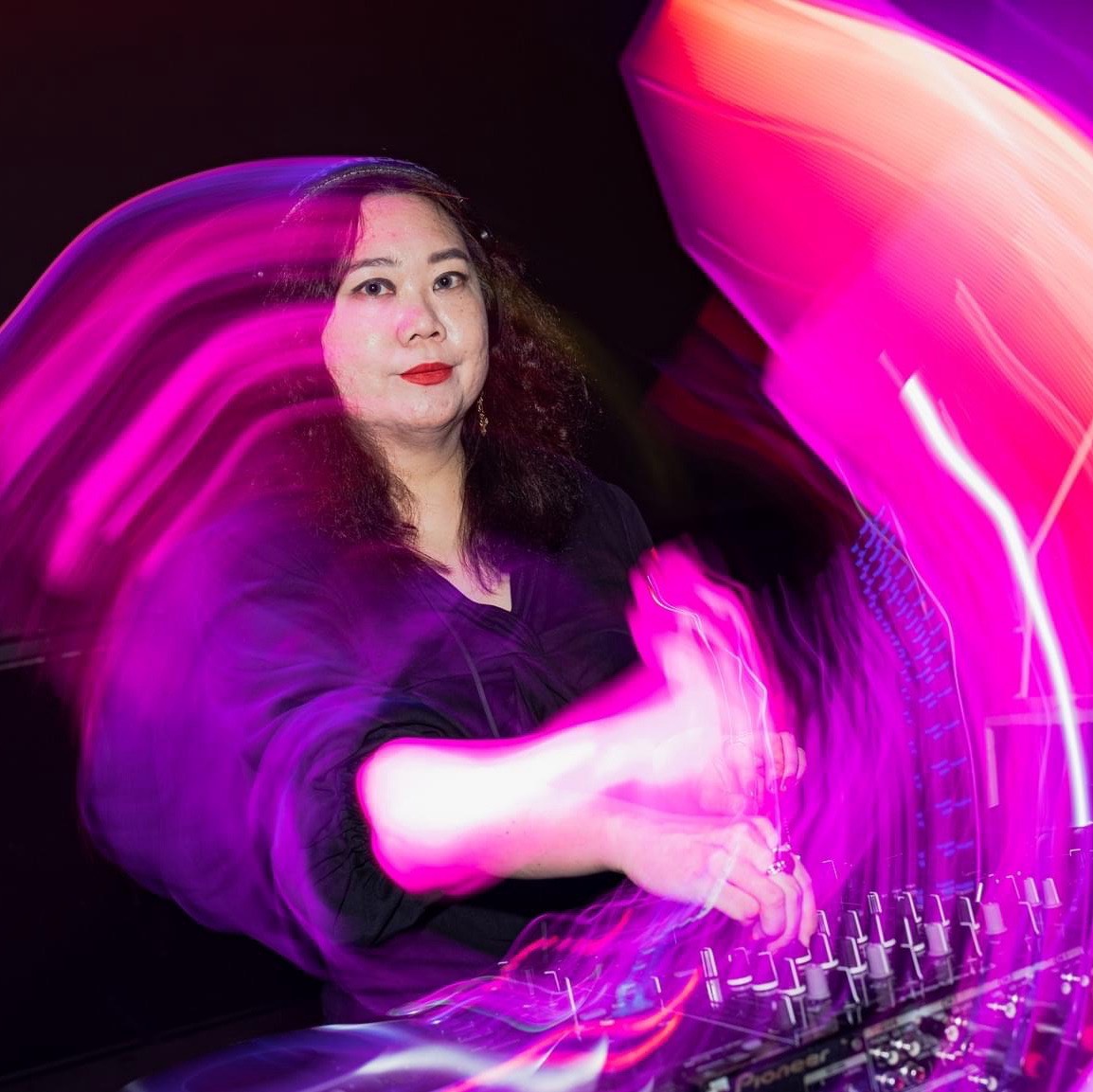 Nhà DJ người Đài Loan Ingry biểu diễn tại một sự kiện, tay phải đặt trên bàn trộn âm thanh, nhìn vào máy ảnh và tập trung trong một hình ảnh màu với những vòng xoáy.