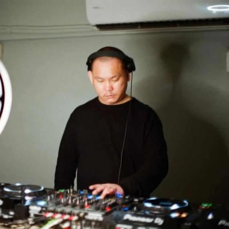 Taiwanese DJ Neil performing on Pioneer CDJs at an event, colour image blurred.
