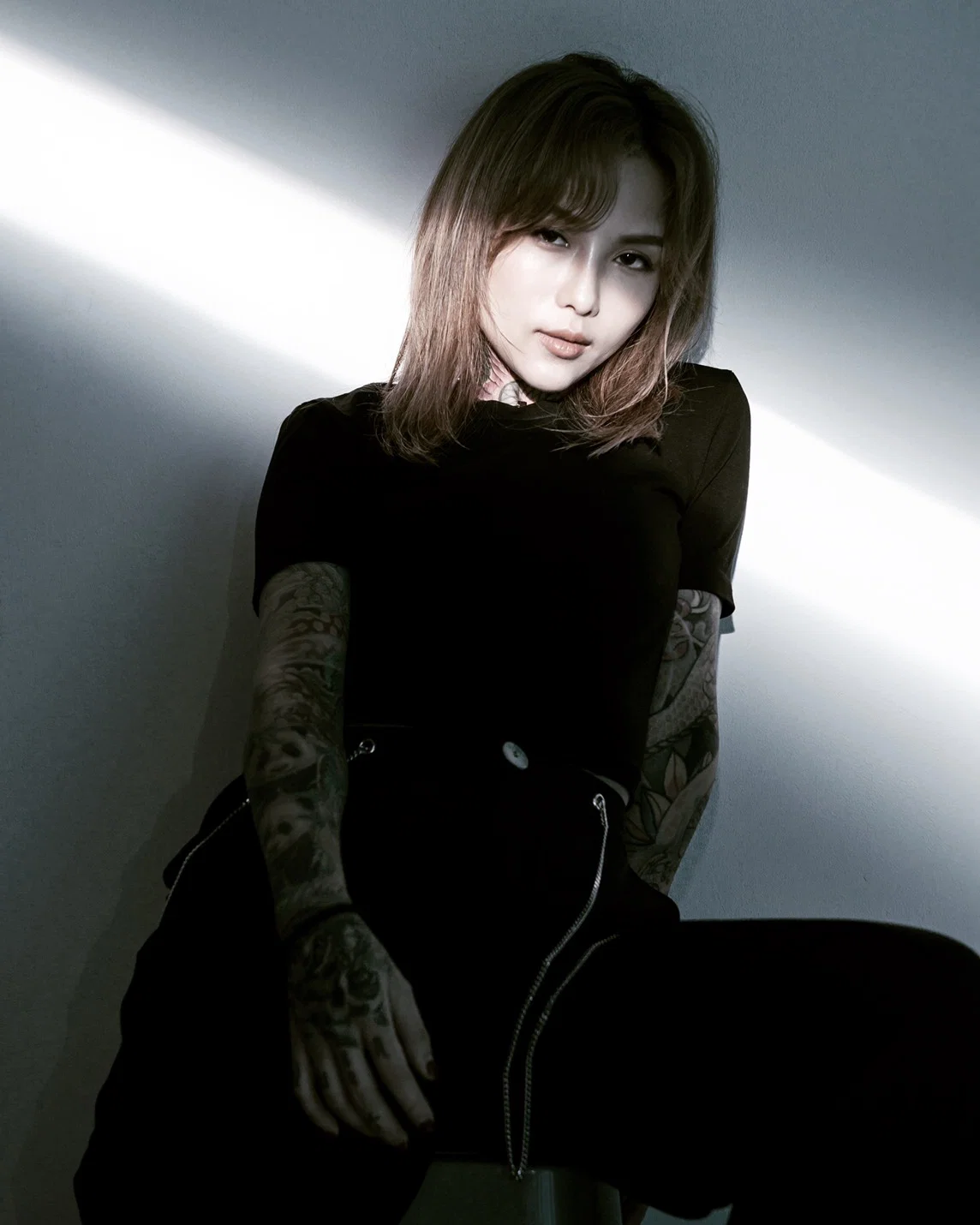 Portrait of Taiwanese DJ and producer DJ HER, also known as Chen Her, seated against a wall with dramatic light and shadow, representing her work across house, techno, melodic house and tech house.