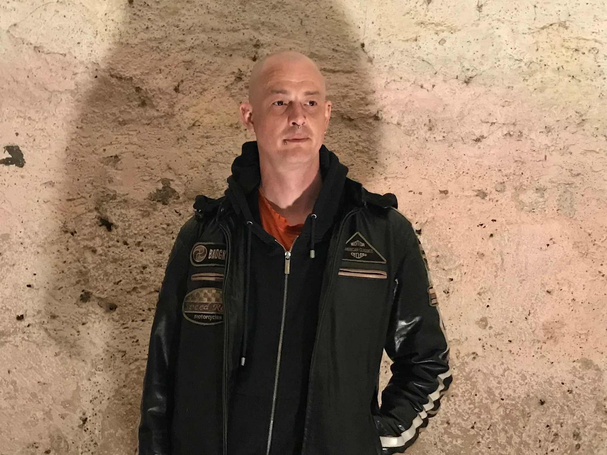 German Dj and producer Chris van Deer standing against wall wearing a coat, colour image.