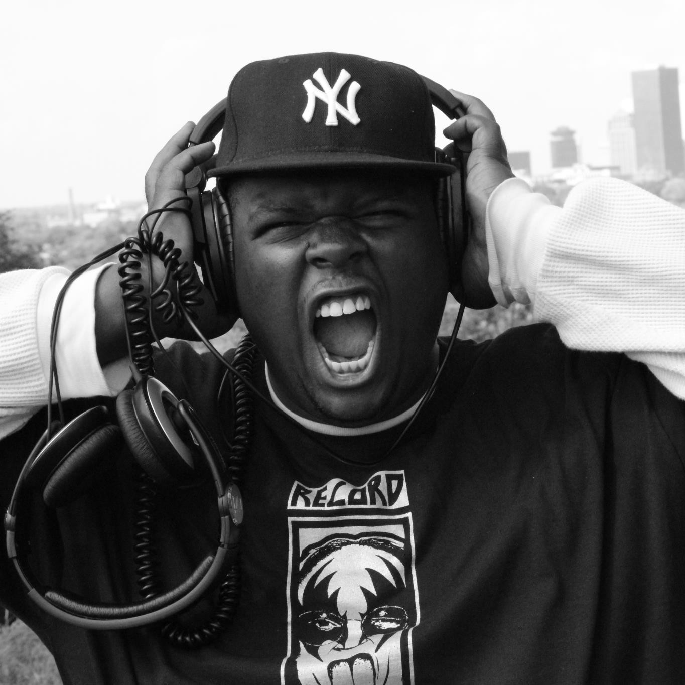 Rapper và nhà sản xuất người Mỹ Kidd Called Quest đội mũ bóng chày của New York Yankees và đeo tai nghe, trong khi một bộ tai nghe khác vắt qua tay phải của anh. Cả hai tay khum lại ôm lấy chiếc tai nghe trên đầu, trong lúc anh hét vào ống kính trong một bức ảnh đen trắng nổi bật.