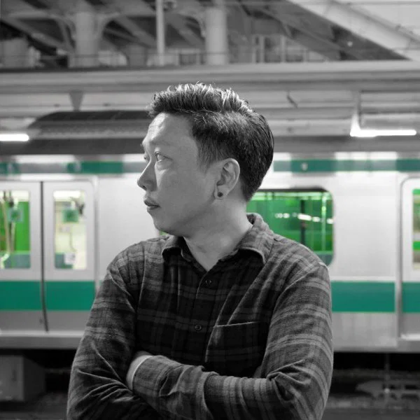 Portrait of Thai DJ and producer Q Narongwate standing with crossed arms at a train station, representing his Deep House and Soulful House sound.