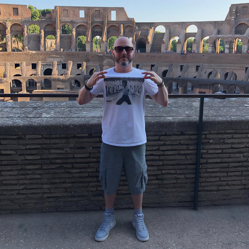 Portrait of Confidence, hip hop producer and artist from Boston, Massachusetts, wearing sunglasses and a Bruce Lee T-shirt while standing in front of the Colosseum.