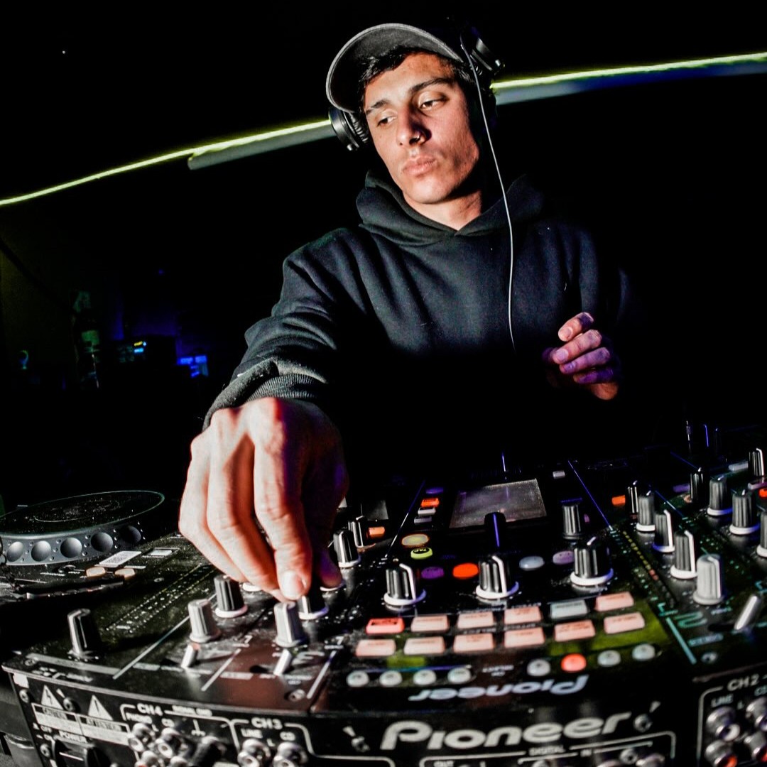 Argentinian DJ and producer Mati Melgarejo is performing live on Pioneer DJ equipment, adjusting the mixer during a dark club set with focused lighting and electronic music atmosphere.