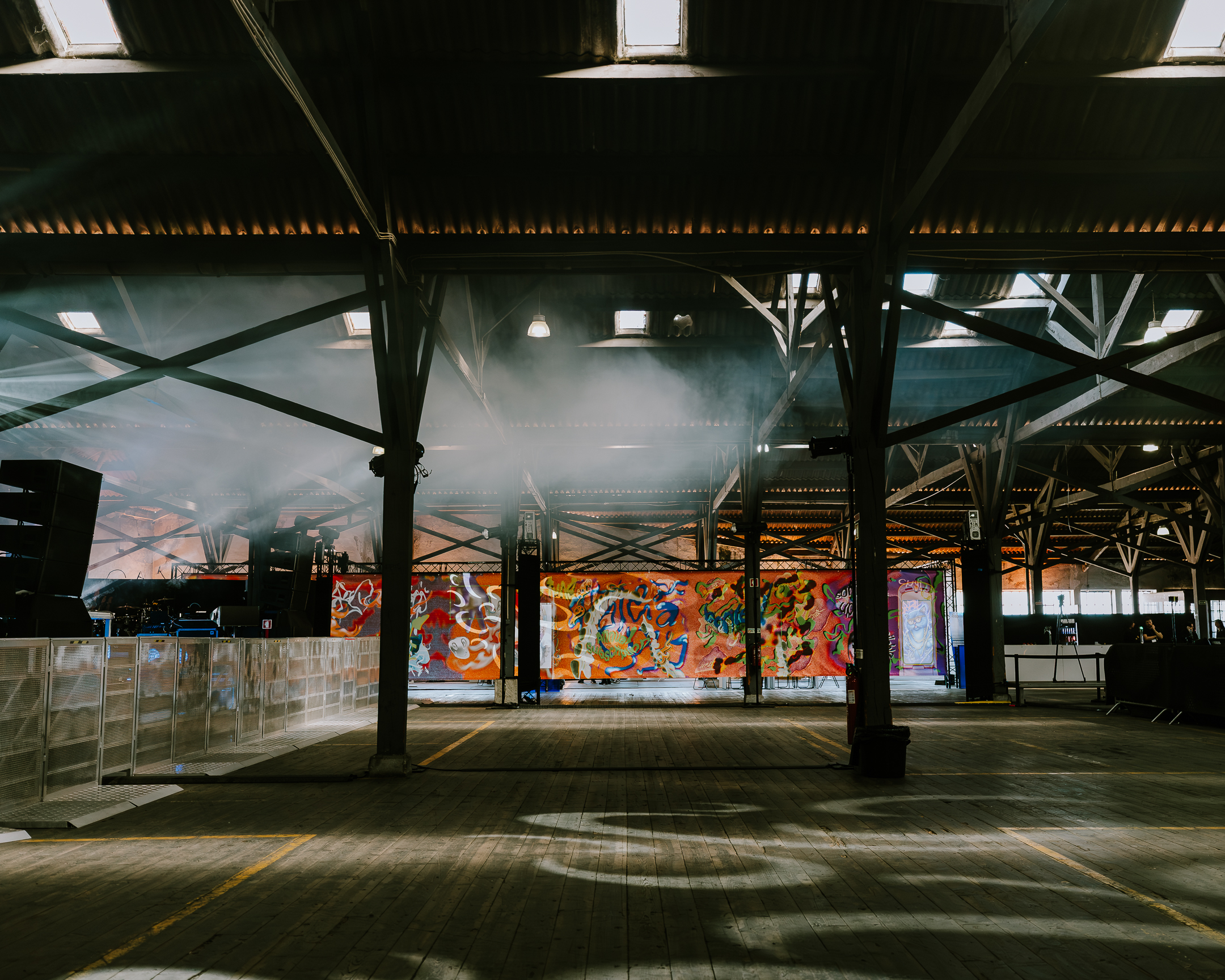 Wide view of the empty Parallel Society 2026 venue in Lisbon before the event, showing an industrial warehouse interior with smoke effects, lighting rigs and colourful mural artwork.