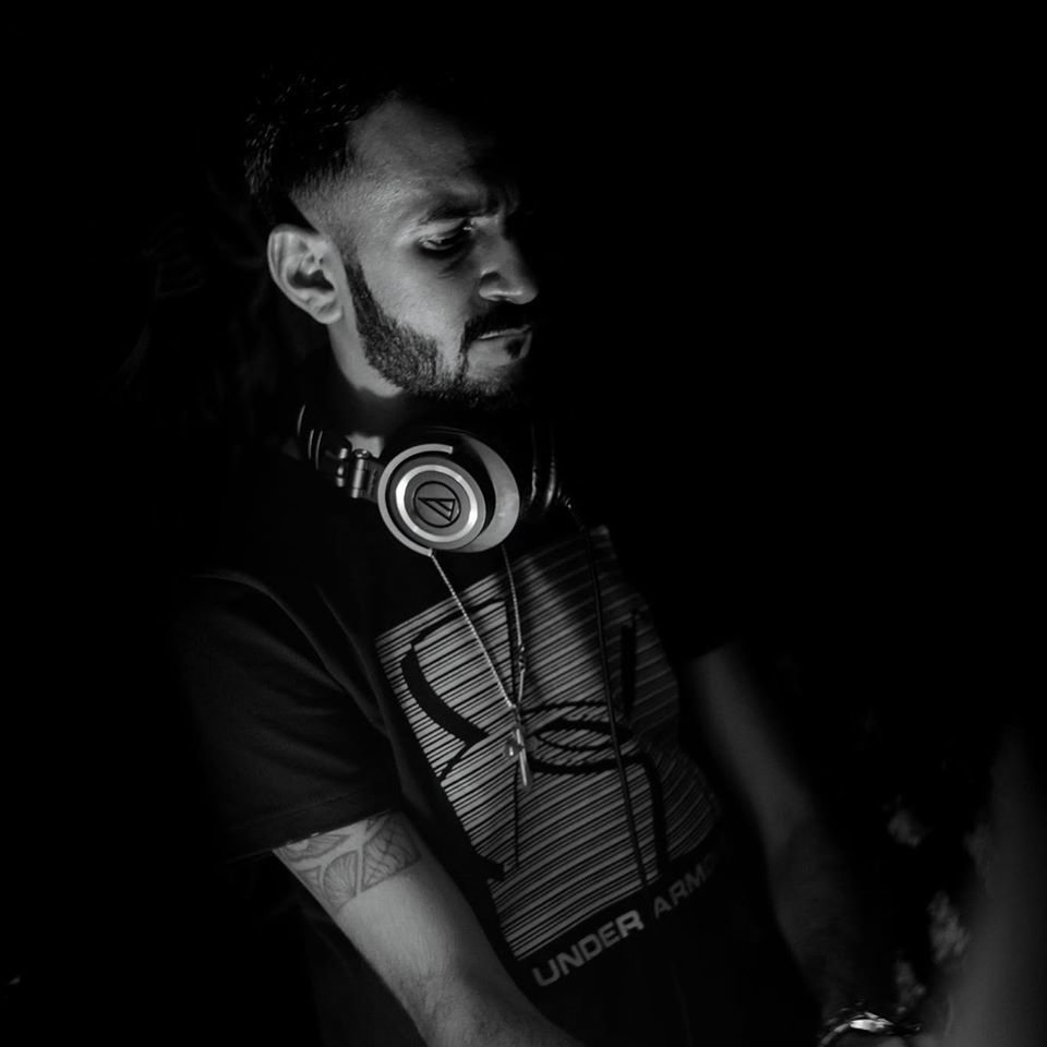 Sri Lankan DJ and producer Praveen Jay performing as dj with headphones around his neck looking down at CDJs, black and white.