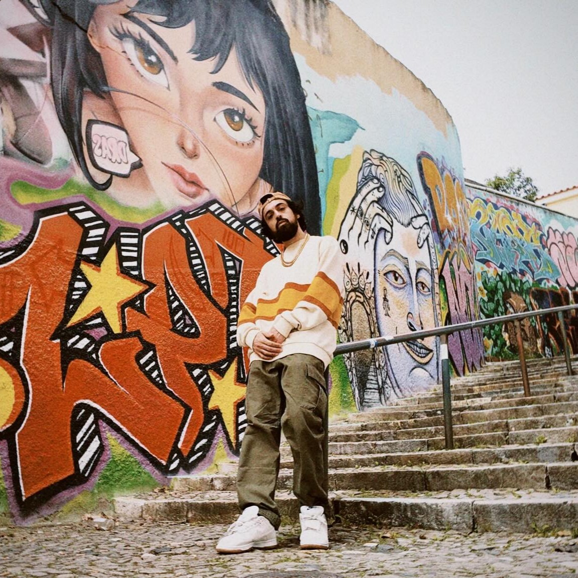 New York lyricist Shah Leezy stands in front of a colourful graffiti wall, representing his underground Hip Hop sound and Staten Island rap connections.