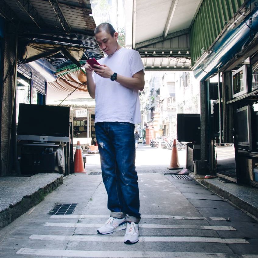 Taiwanese DJ and producer Murphy Kin playing with his phone whilst standing, colour image.