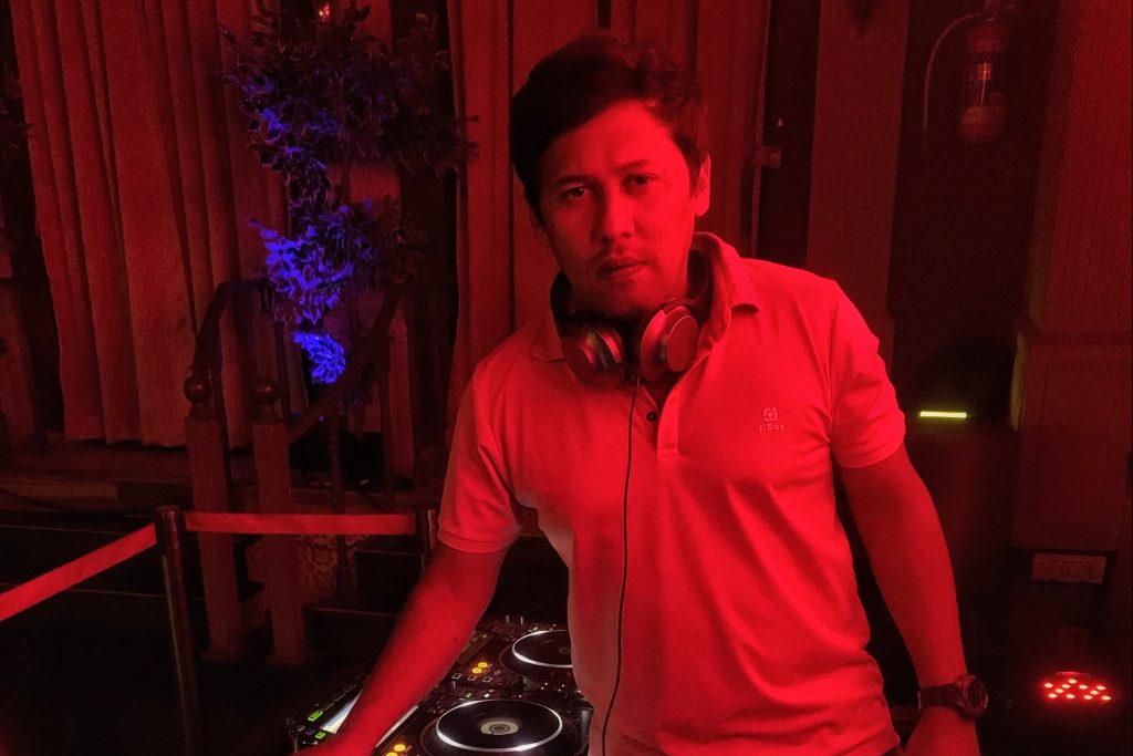 Indian DJ Psy Inertia performing at an event with red lighting, colour image.