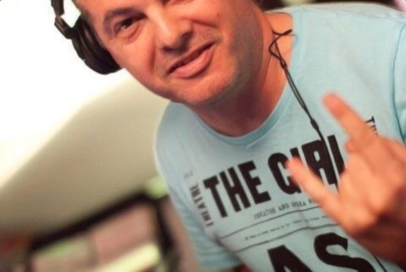 Italian DJ and producer Marco Mei wearing headphones with two fingers up on his left hand smiling at camera, colour image.