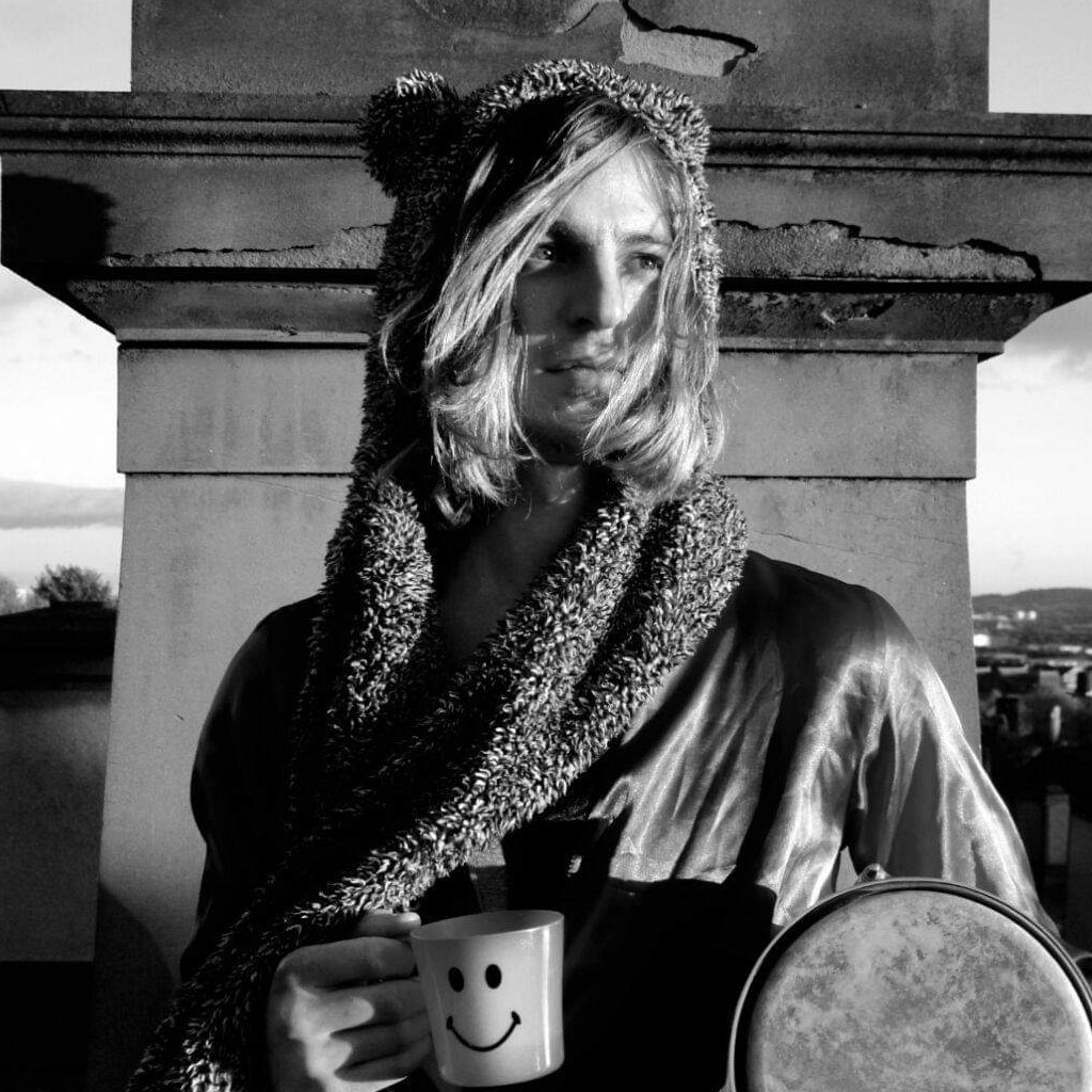 British DJ and producer Ezmun standing in front of monument holding a mug with a smiley face, image in black and white.