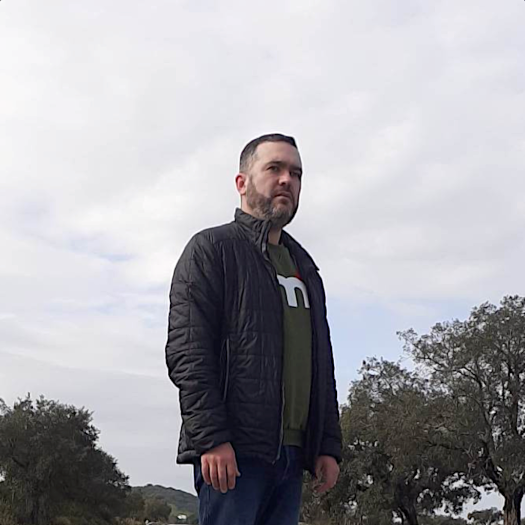 Portuguese DJ Joshua standing in the countryside on a road looking up to the left, colour image.