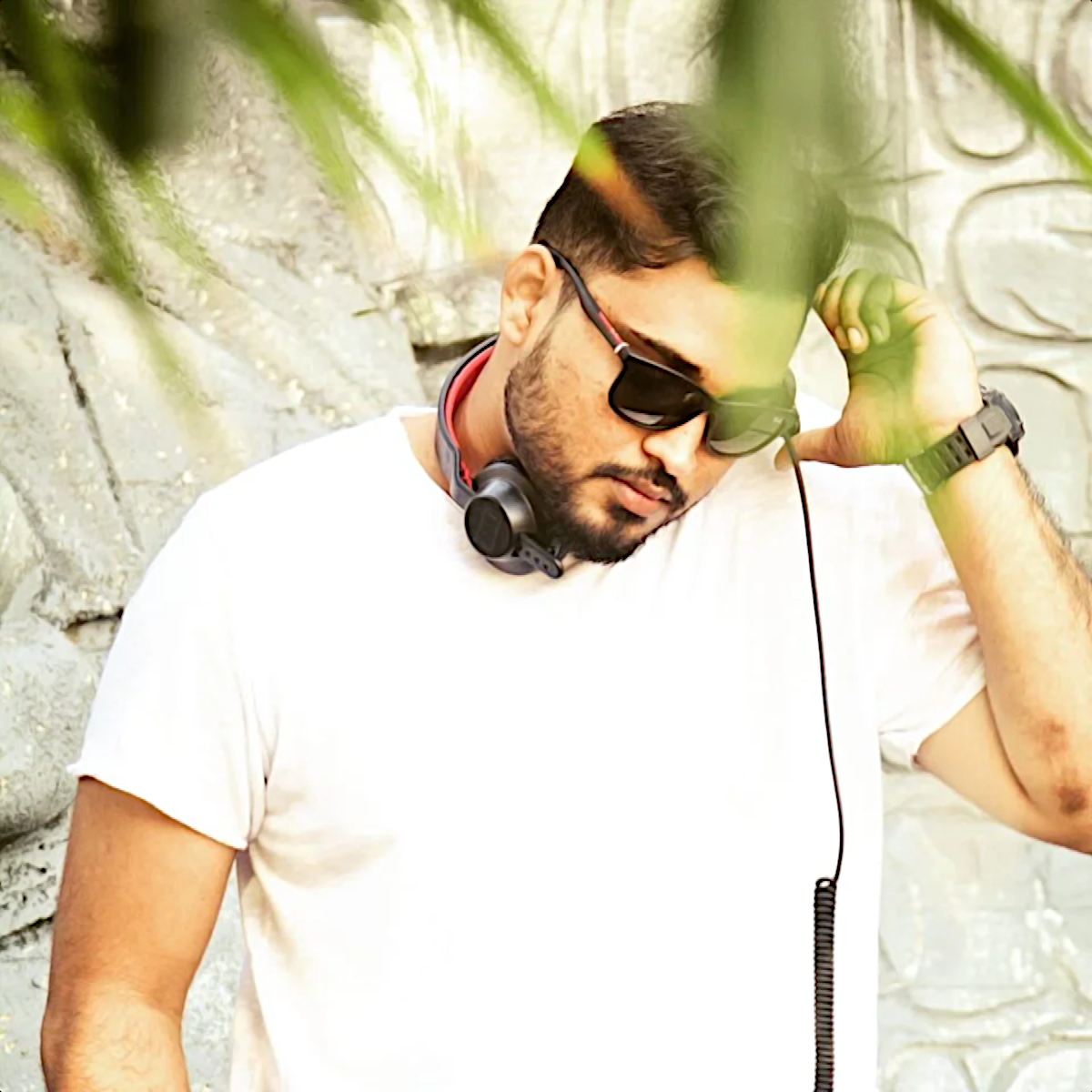 Sri Lankan DJ and producer VegaZ wearing sunglasses and headphones around his neck whist scratching his head, colour image.