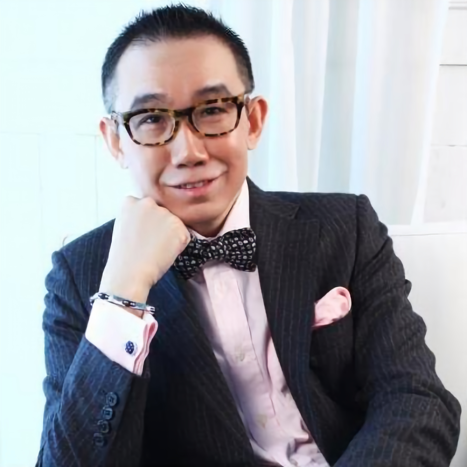Taiwanese DJ Louis Chen sitting in a chair and looking at the camera with his chin on his right hand wearing a dinner suit, colour image.