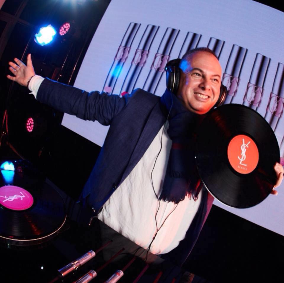 Italian DJ and Producer Marco Mei holding a YSL Vinyl in his left hand and smiling with his right arm outstretched, colour image.