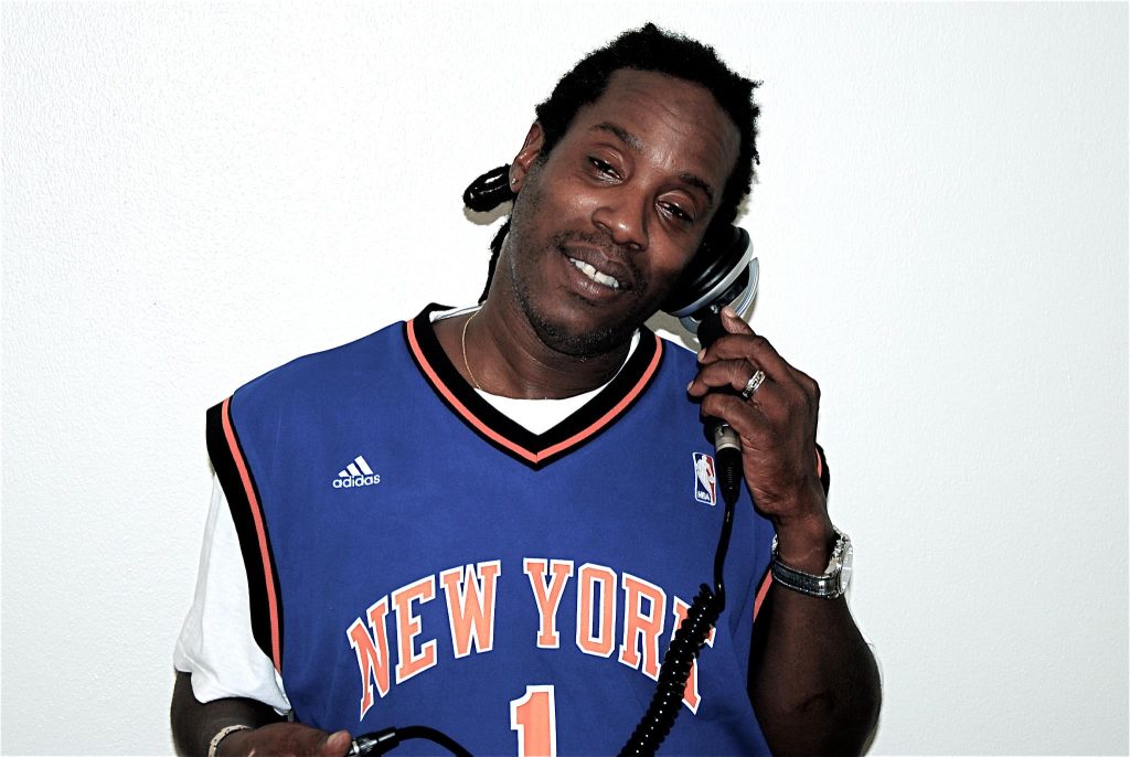 British DJ and producer Bert Bevans holding a monophone to his left ear and smiling, colour image with white background.