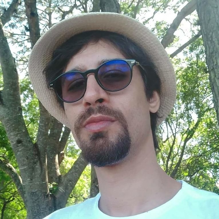 Brazilian DJ and producer Forest Weed wearing a hat and sunglasses standing in Forest, colour image.