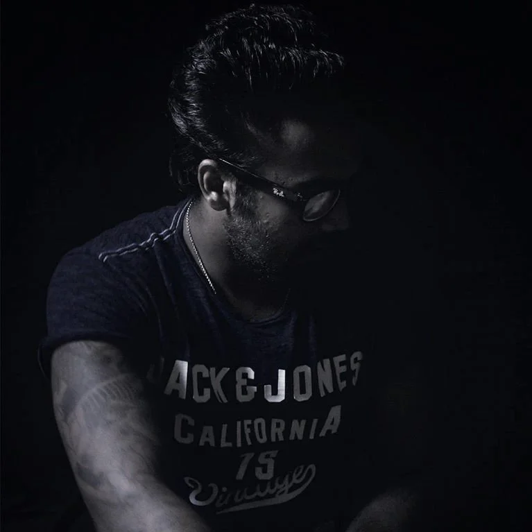Sri Lankan DJ Fernando sat in dark looking left.