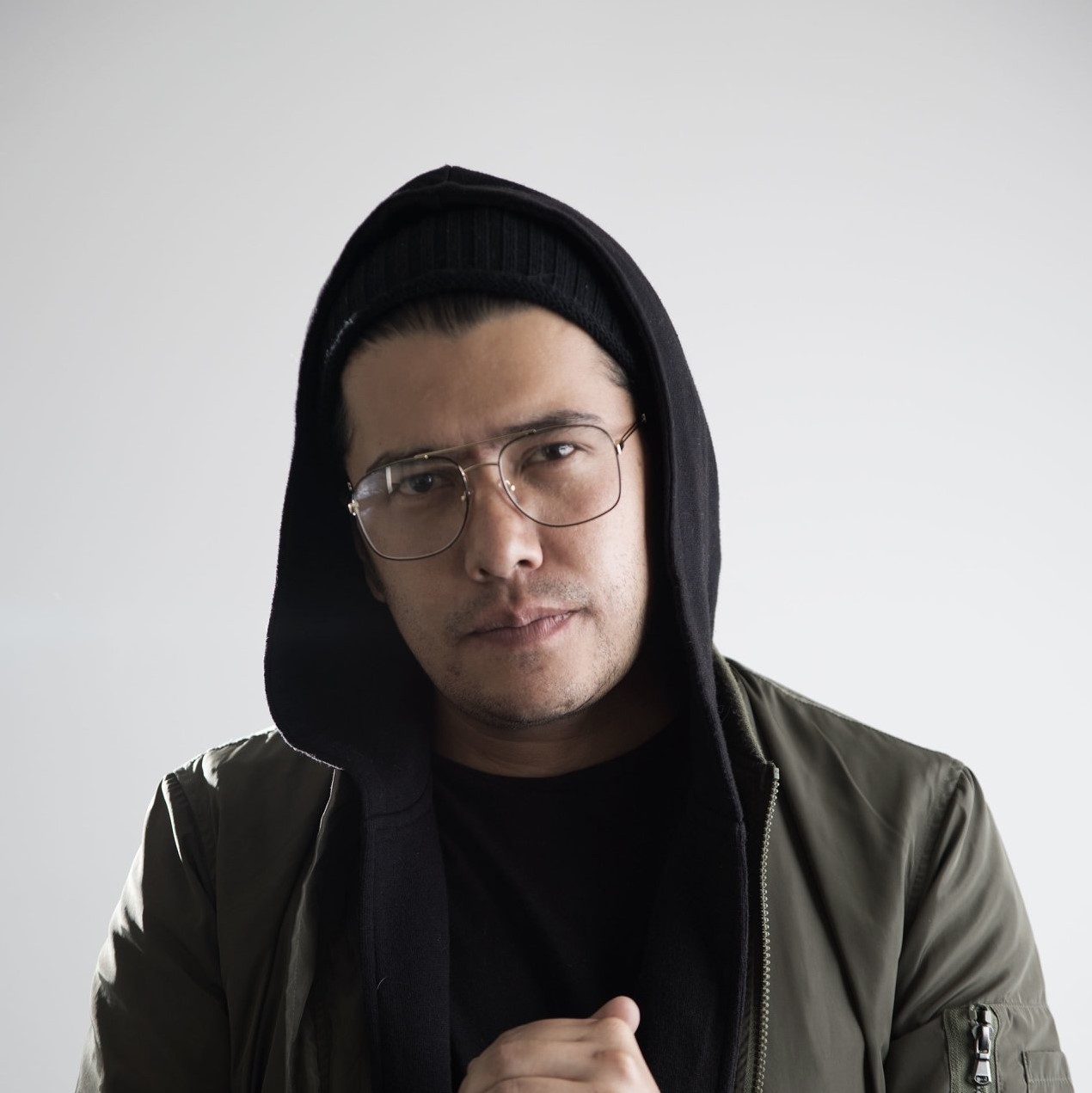 Colombian DJ and producer Creative Machine wearing glasses and a hoodie jacket and looking at the camera in upper body shot, colour image.