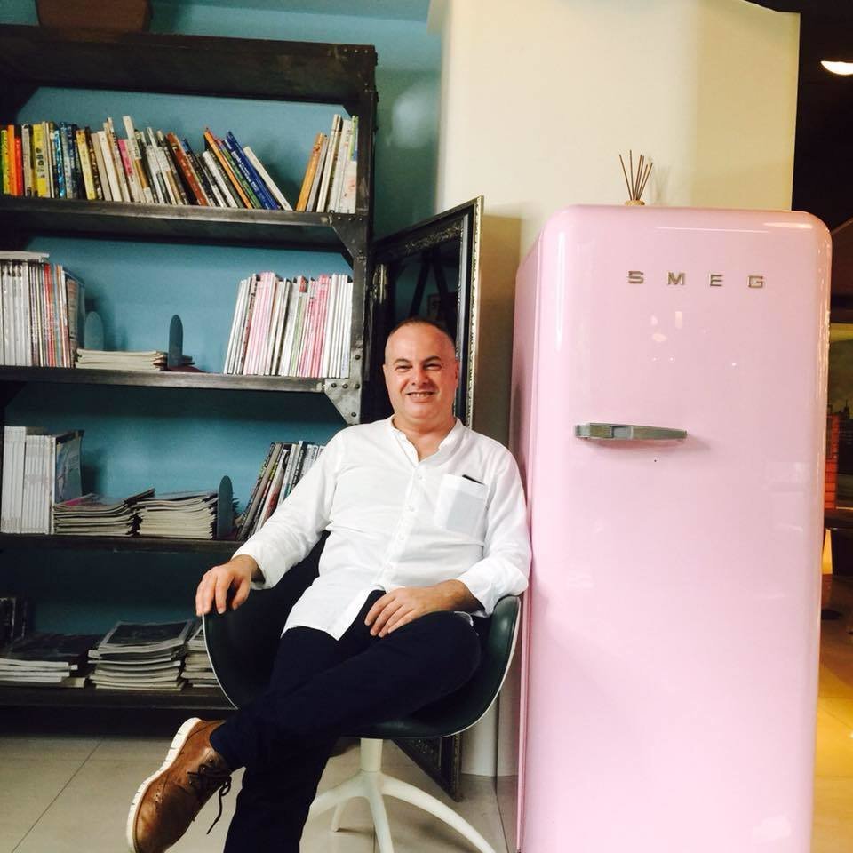 Italian DJ and Producer Marco Mei sitting in chair next to a pink SMEG fridge, colour image.