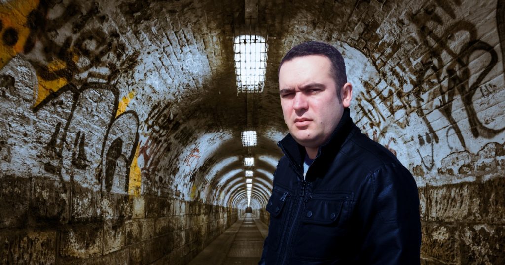 Portuguese DJ Joshua standing in a tunnel covered in graffiti looking at the camera, colour image.