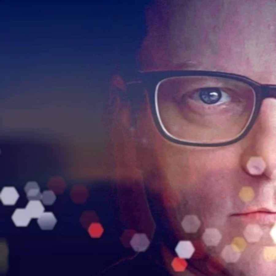 British DJ and producer Gav Easby in a close-up shot, wearing glasses, showing the right side of his face as he stares straight ahead, with a hexagonal lighting effect in a color image.