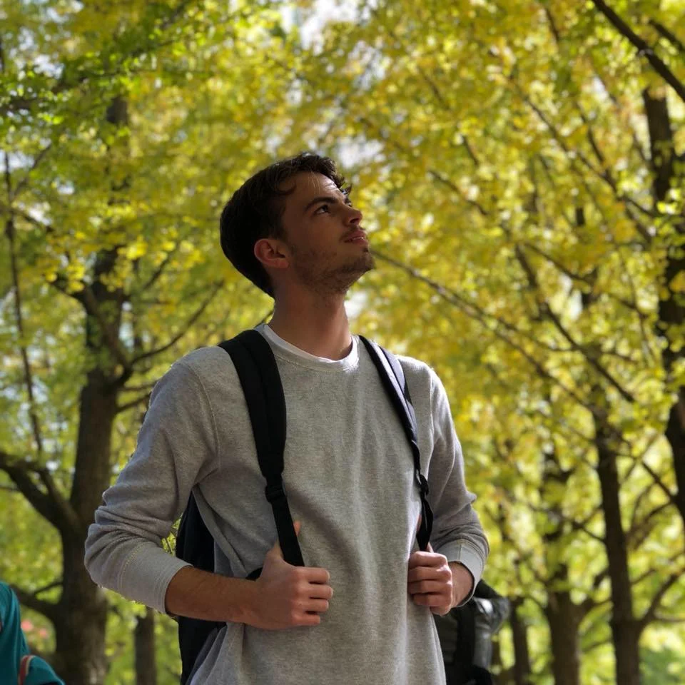 Swiss DJ Marc Küng standing in forest wearing rucksack looking up at the sky, colour image.