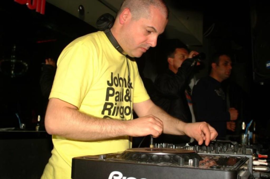 Italian DJ and producer Marco Mei performing at an event wearing a yellow T-shirt, colour image.