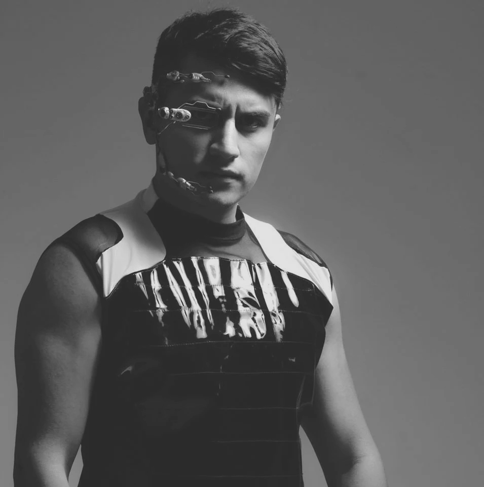 Stephan Govarg in futuristic attire with metallic facial accessories poses against a gray background. The image is in black and white, conveying a serious mood.
