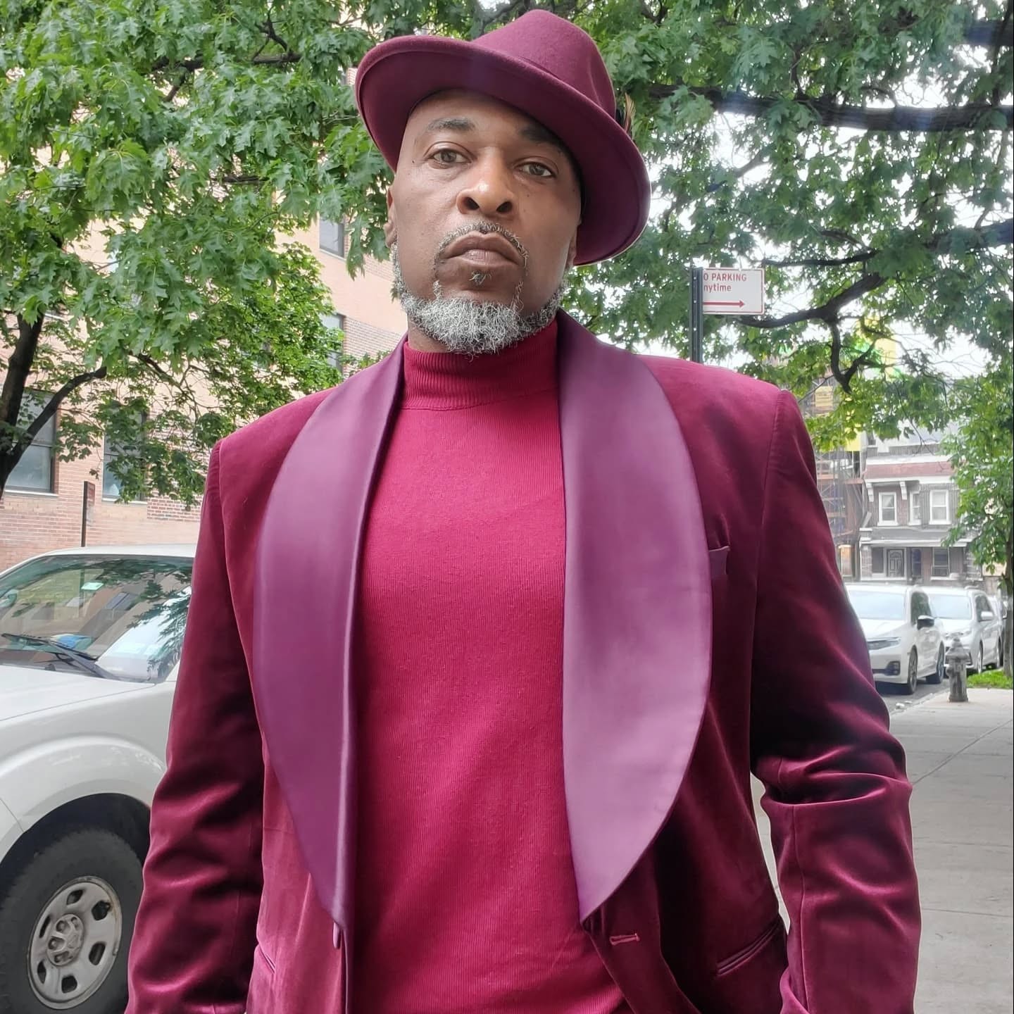 In the picture, American rapper Thunny Brown is wearing a purple suit and hat, he is looking directly at the camera with a serious look in this colour image.