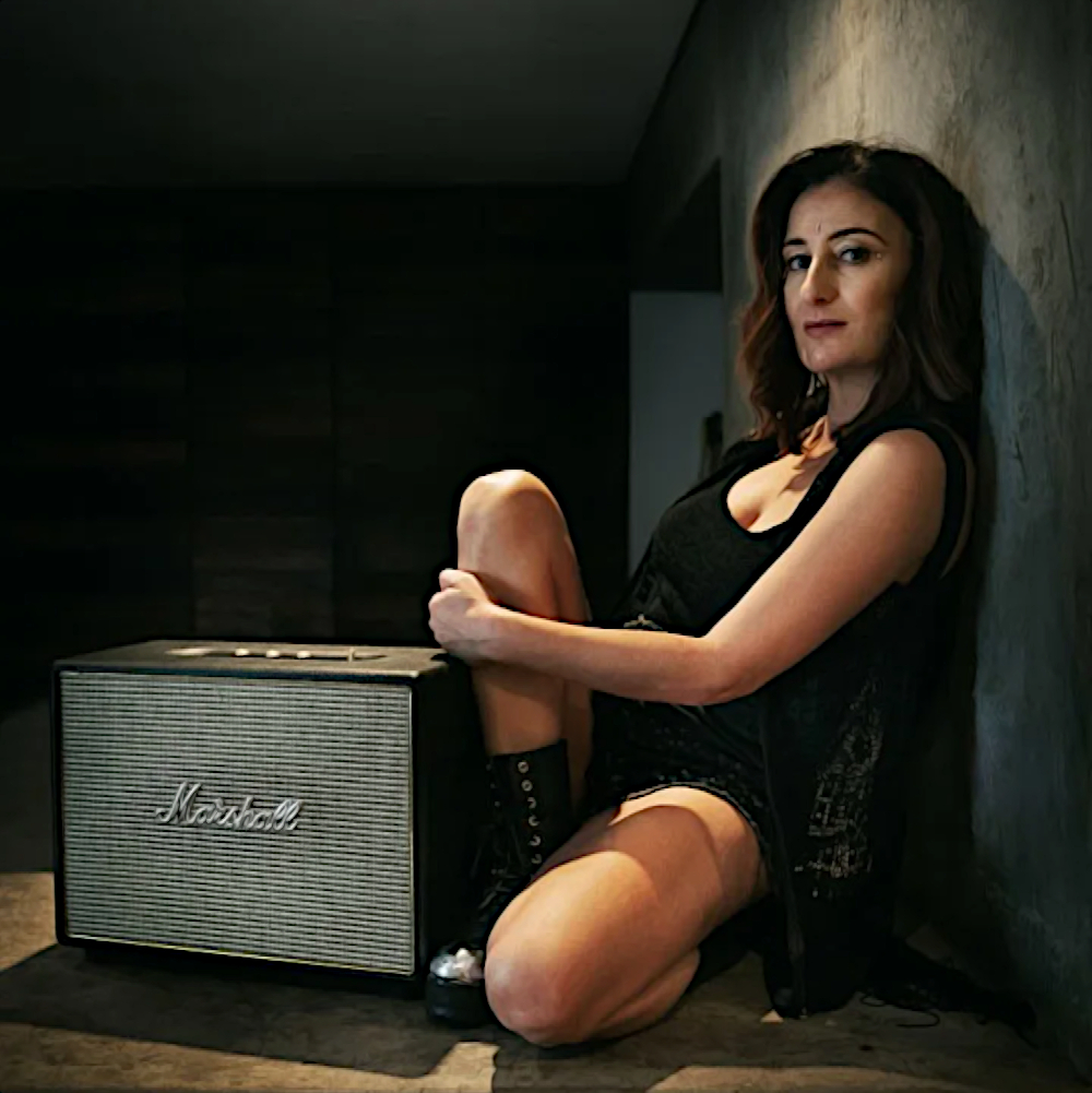 South African DJ ASH sitting beside a Marshall Guitar amplifier looking at camera, colour image.