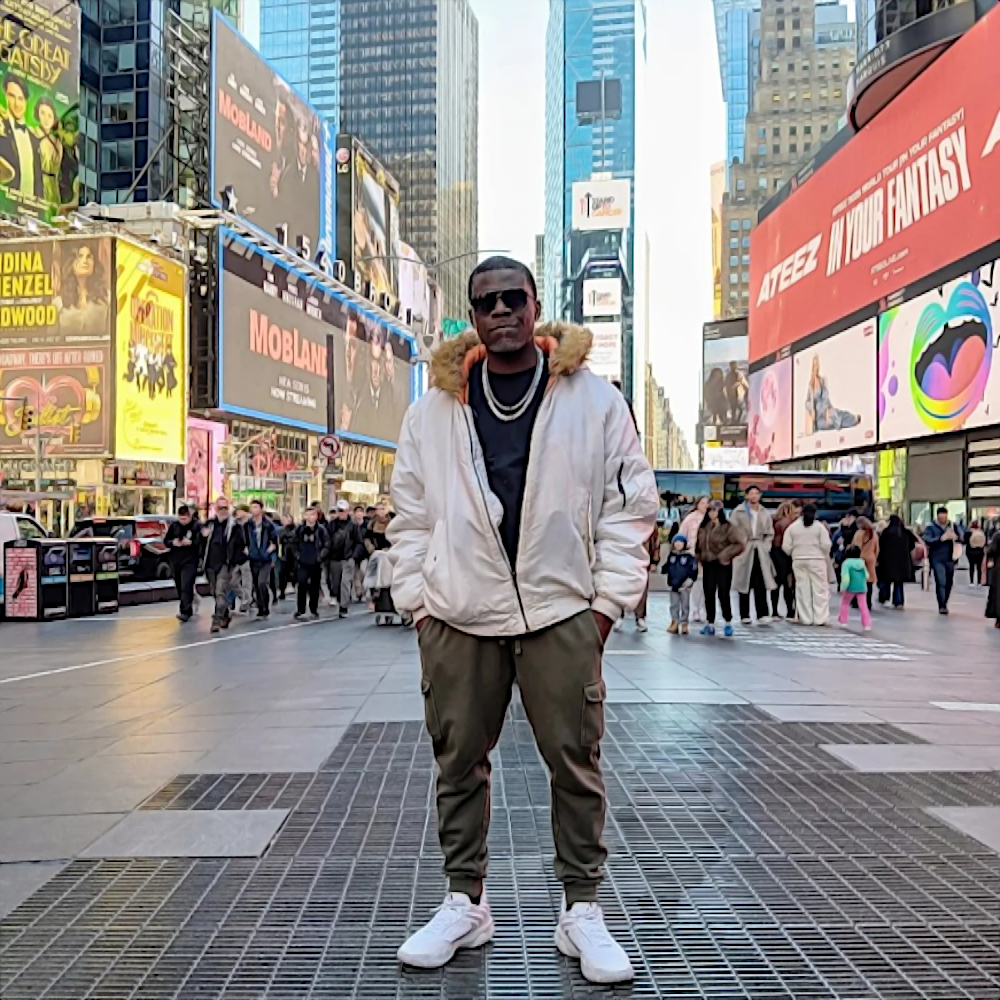 American rapper Lex Lakaiser standing in a street in New York, USA wearing sunglasses and a beige warm jacket and white sneakers, with his hands in the pockets of his pants, colour image.