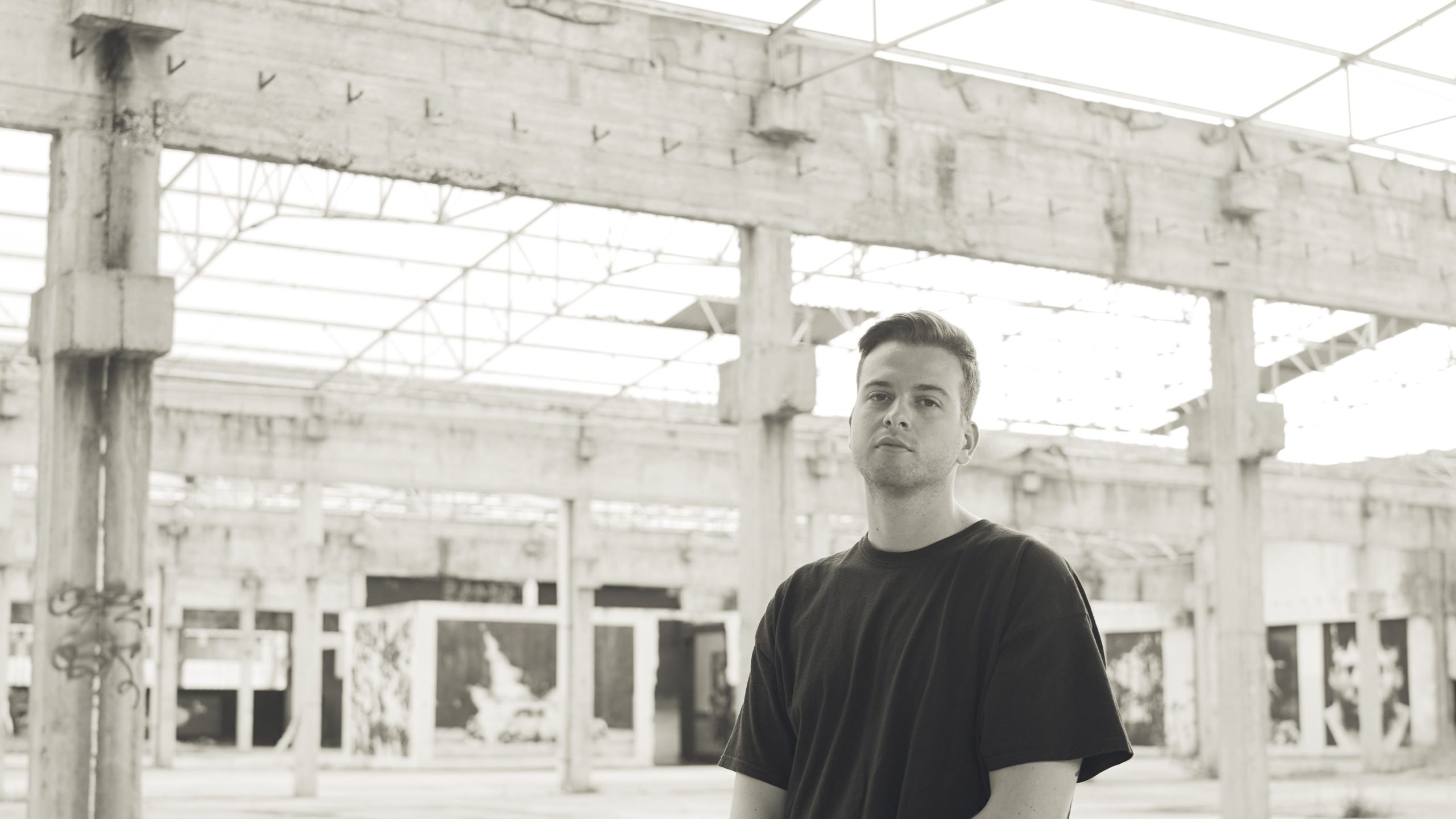 Greek DJ and producer Toquito standing in empty building looking at camera, black and white image.