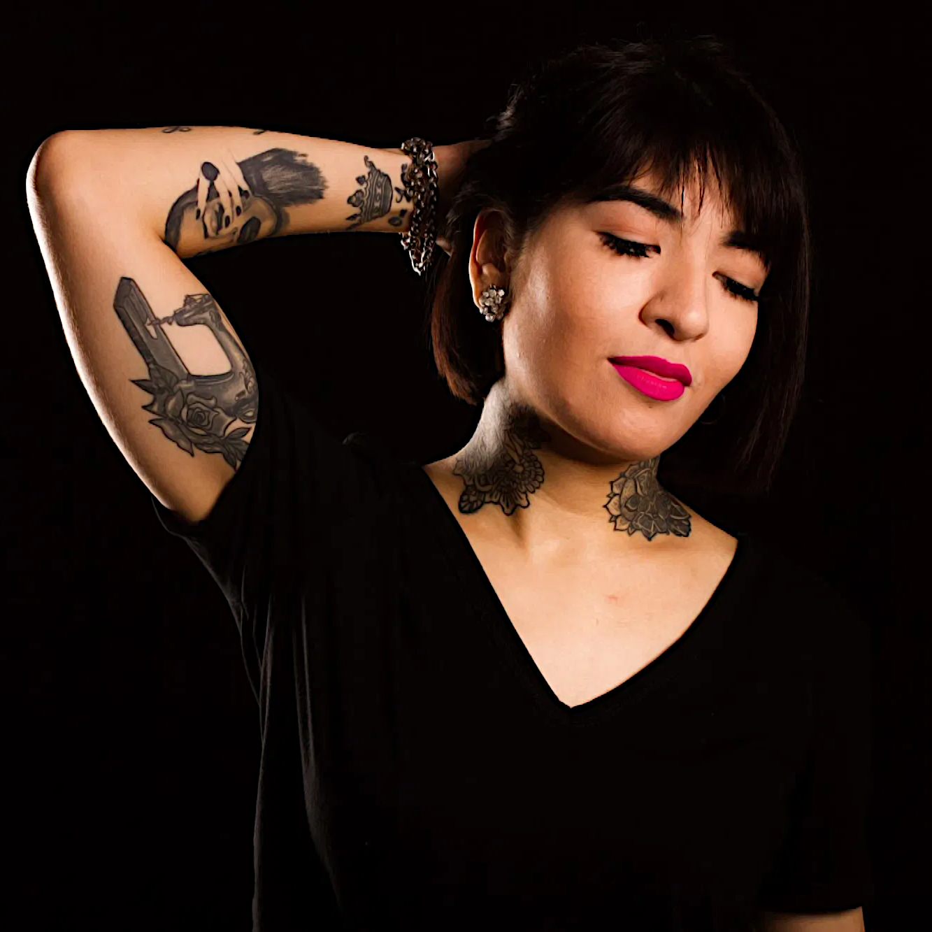 Argentinian DJ Yamila Charpentier with her right hand behins her head showing tatoos on her arm and neck in blackened room, colour image.