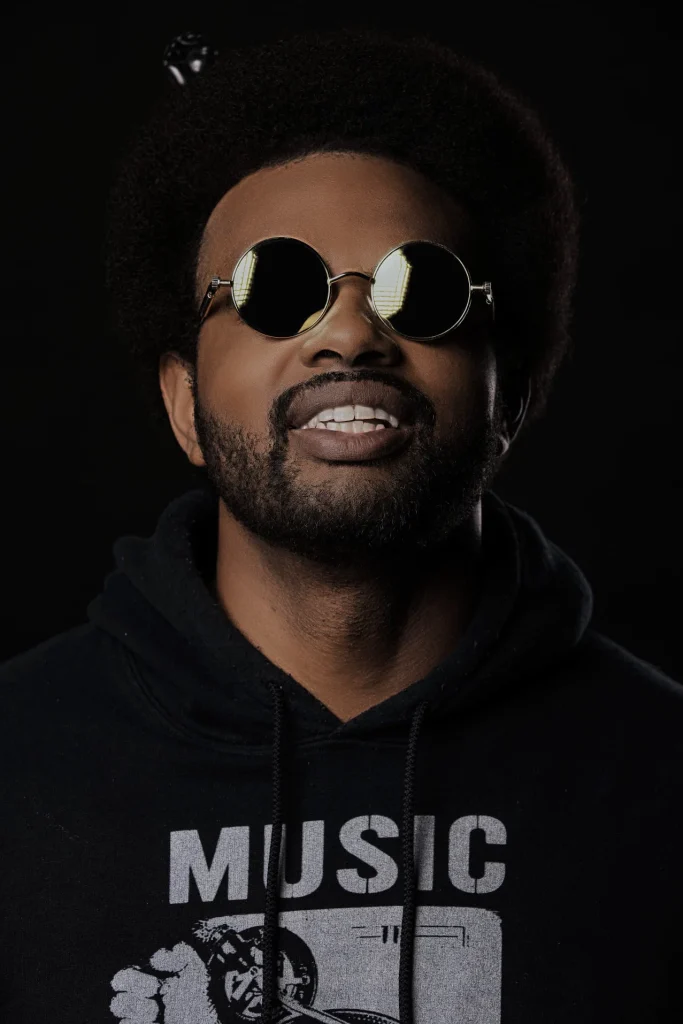 Portrait of Digital D, also known as DaTron King, wearing round sunglasses and a black hoodie, representing his Deep House sound and work across the Taipei underground scene.