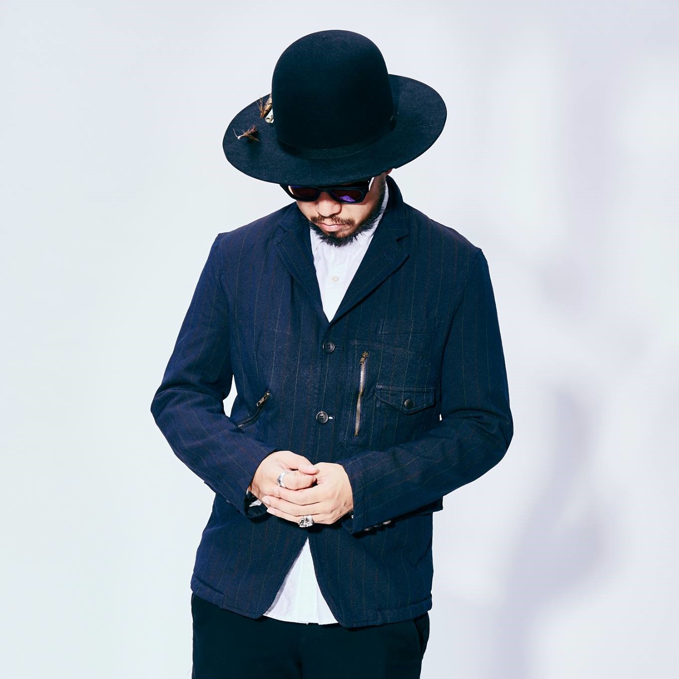 Thai DJ and promoter Supersonic wearing a hat and sunglasses leaning forward with his head down, colour image.