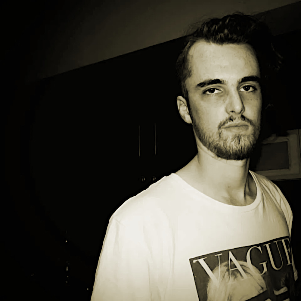 Australian DJ Cru Kza standing to the left of the picture looking at camera in upper body shot, black and white image with beige tinge.