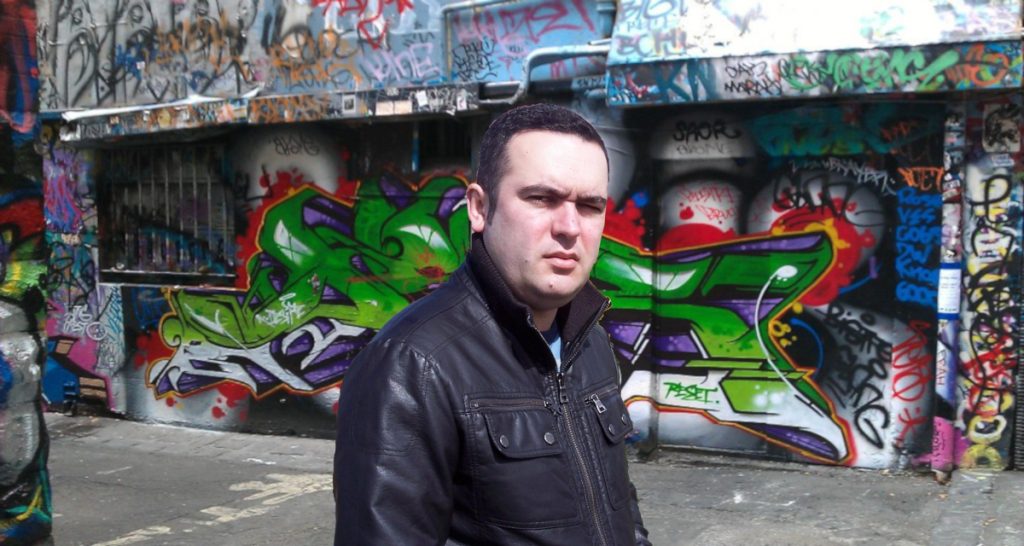 Portuguese DJ Joshua on a street in Melbourne, Australia stading in front of a graffiti wall, colour image.