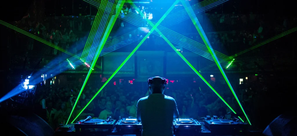 British DJ and producer Graham Gold performing at Peach in London, standing behind the decks in front of a packed crowd with green laser lights crossing above the dancefloor.