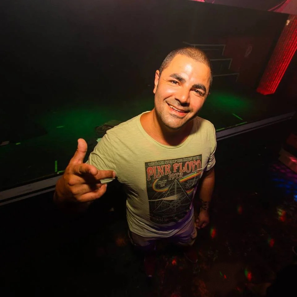 Nhà sản xuất và DJ người Đức Benito Blanco đứng mỉm cười trước ống kính trong một địa điểm, tay trái đút trong túi quần, tay phải giơ lên chào kiểu súng lục trong một bức ảnh màu.