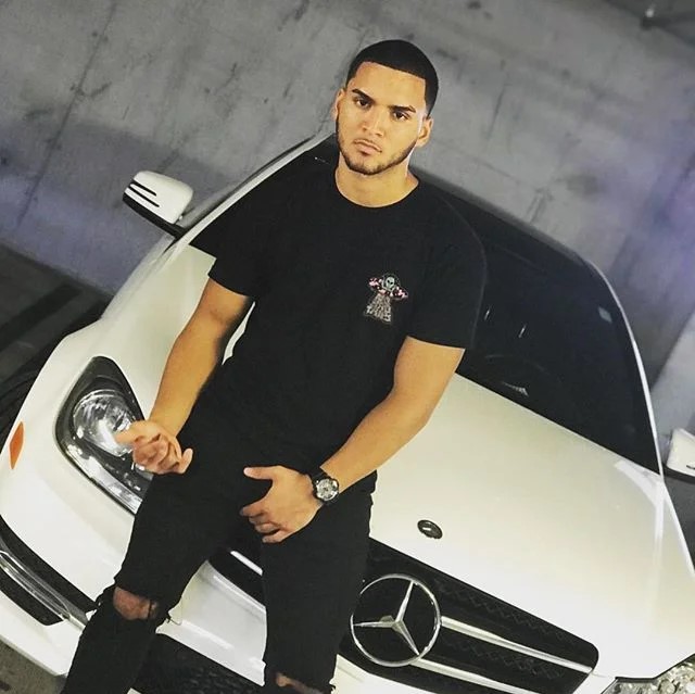 Puerto Rican DJ Kyza leaning against a Mercedes looking at the camera, colour image.
