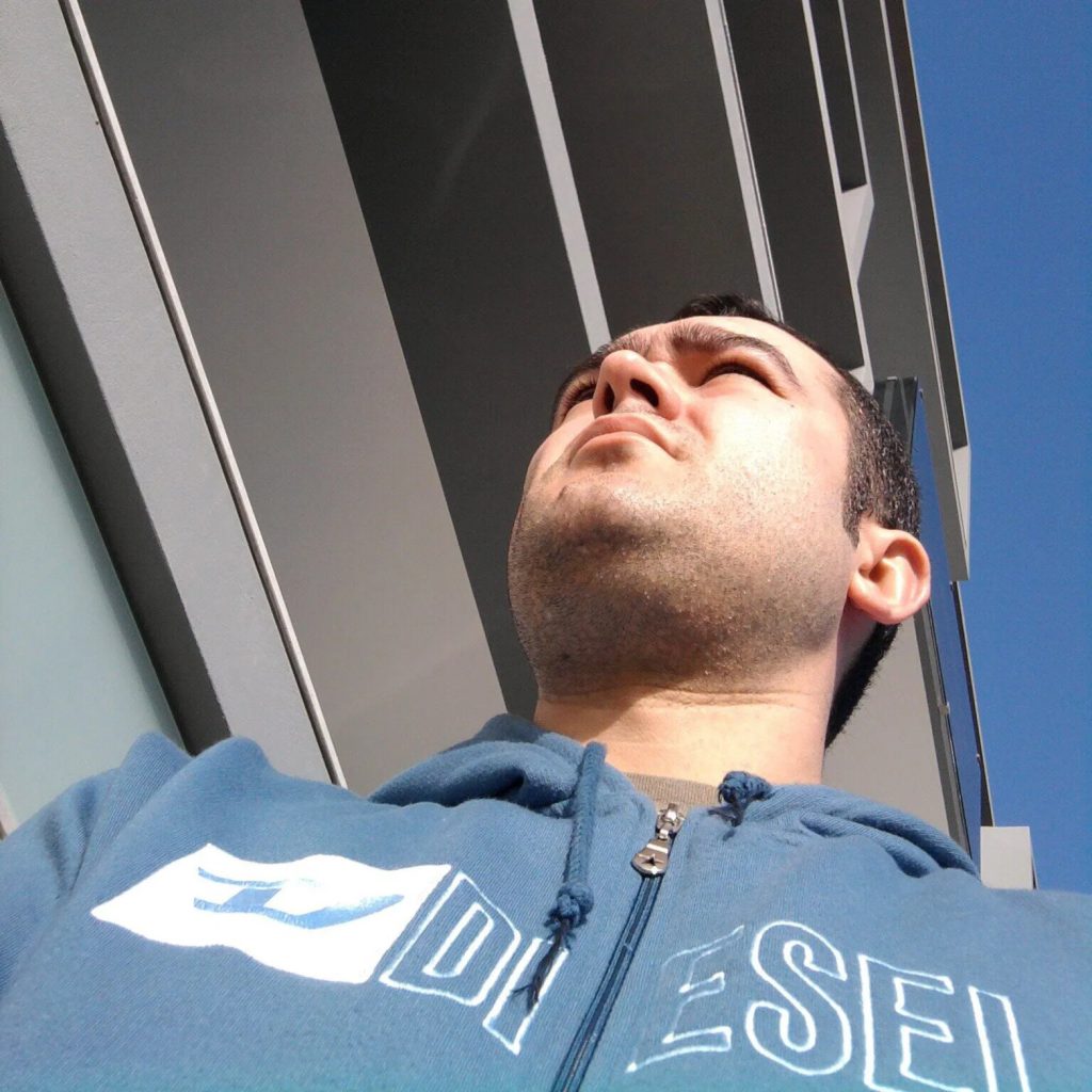 Portuguese DJ Joshua standing with a cmera looking up at his upper body and face, colour image.