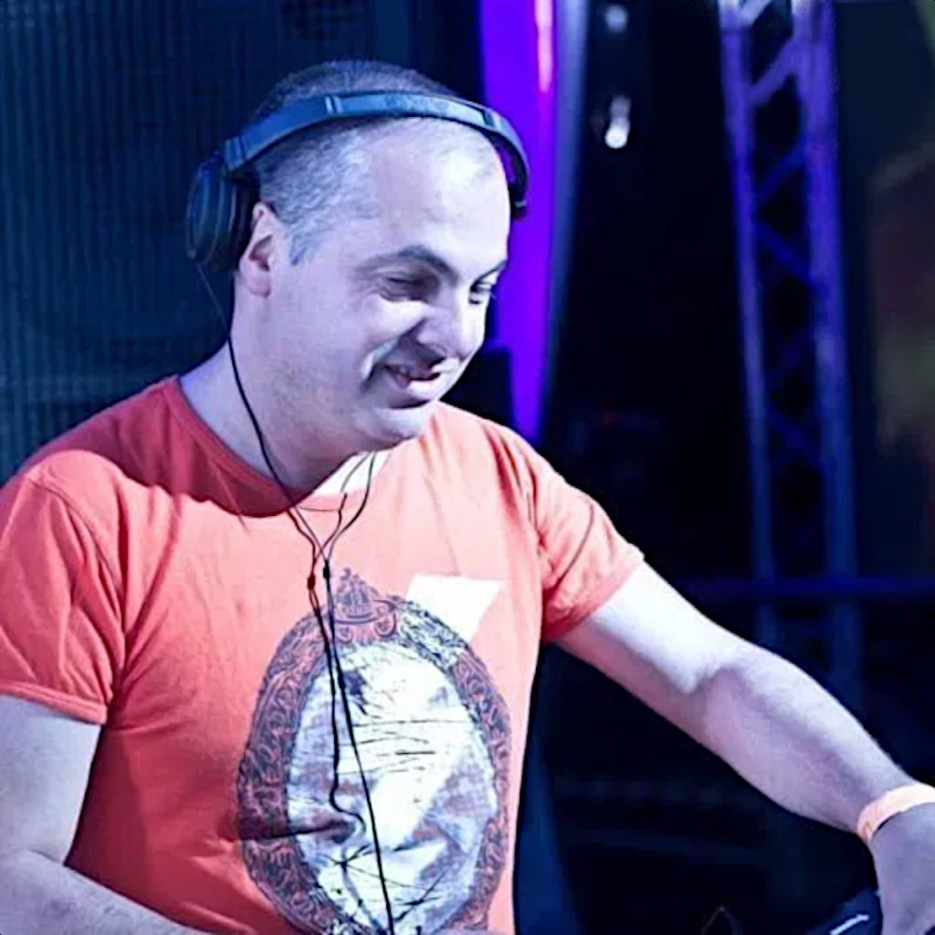 Italian DJ and producer Marco Mei performing at an event in Russia, wearing a orange T shirt and headphones and smiling, colour image.