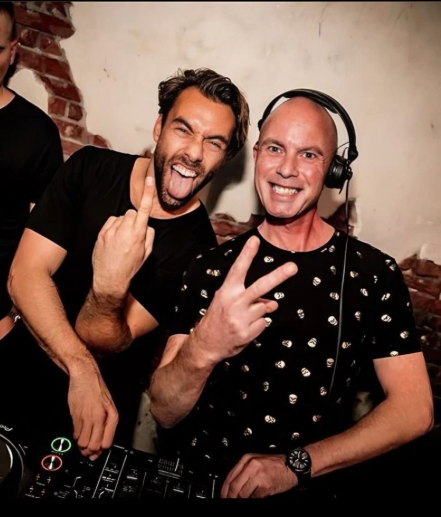 Dutch DJs Reinoud van Toledo and Jack Delhi pose together behind a DJ setup, representing their shared connection through Amsterdam’s underground electronic music scene.
