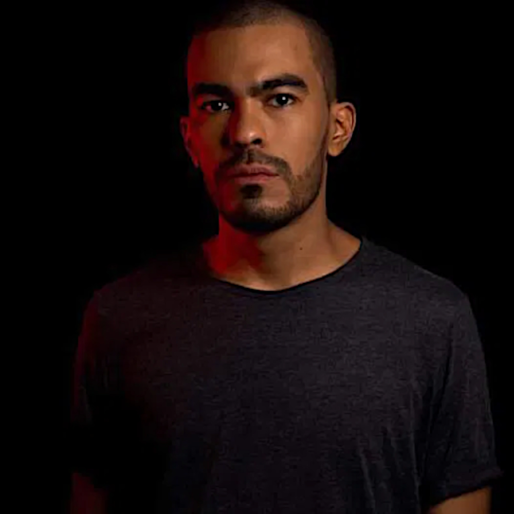 Colombian DJ and producer Gutz looking at camera in a studio shot with a black background, colour image.