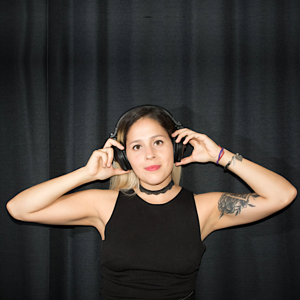 Argentinian DJ and producer Lelus Red wearing headphones with her hands on the cups smiling and looking at the camera in a studio shot, colour image.