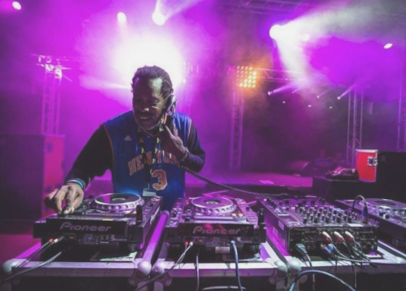 British DJ and producer Bert Bevans performing at an event holding his headphone to his left ear, colour image.