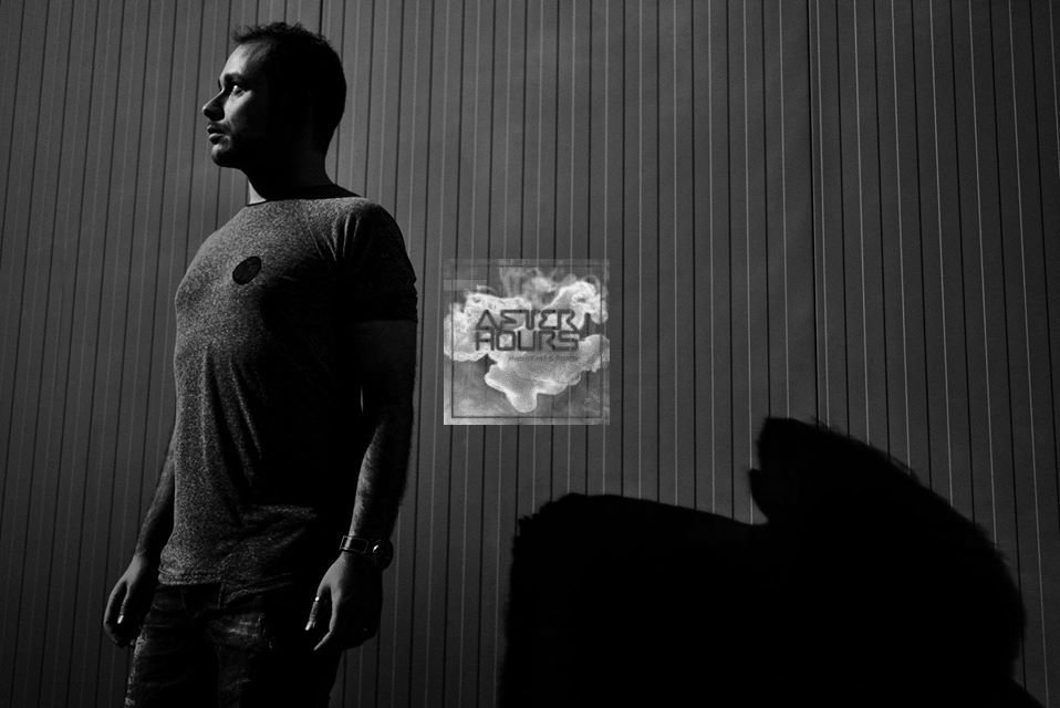 Greek DJ and producer Dimii standing looking to his right is a dark room, black and white photo.
