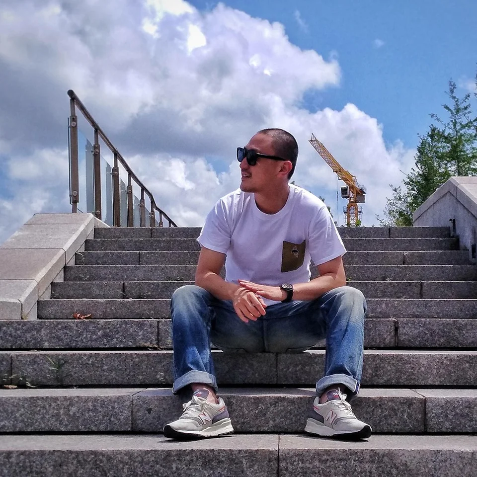 Taiwanese DJ andf label owner Murphy Kin a.k.a DJ Lucy sitting on a step wearing sunglasses and looking to his right, colour image.