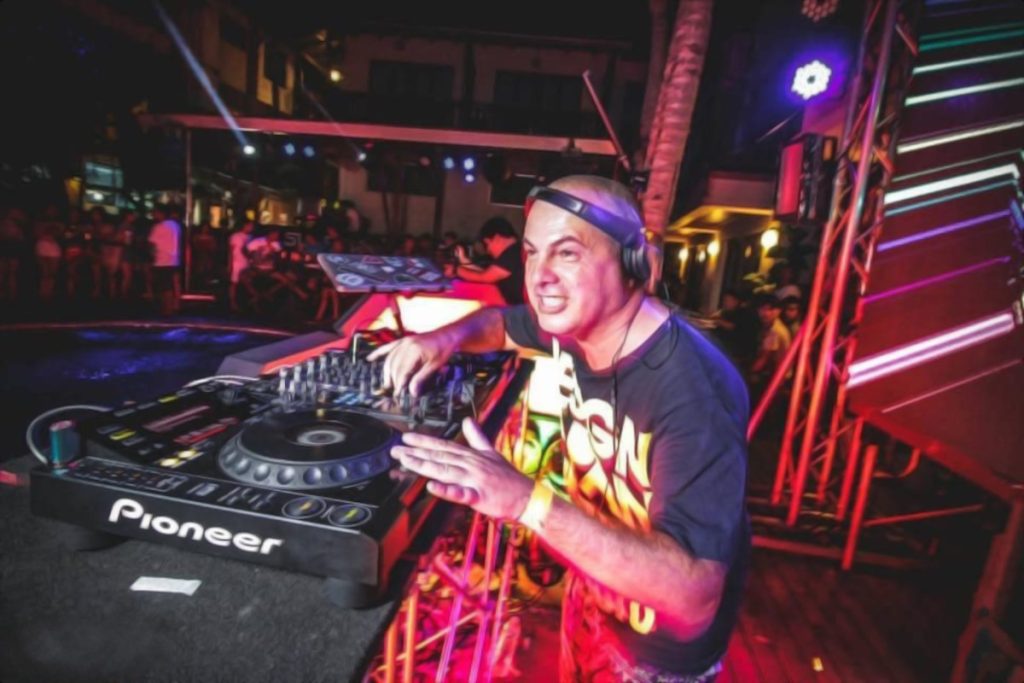 Italian DJ and producer Marco Mei performing at an event at Surf Thailand wearing headphones and looking at the crowd with his hands on the CDJ taken from his left side, colour image.